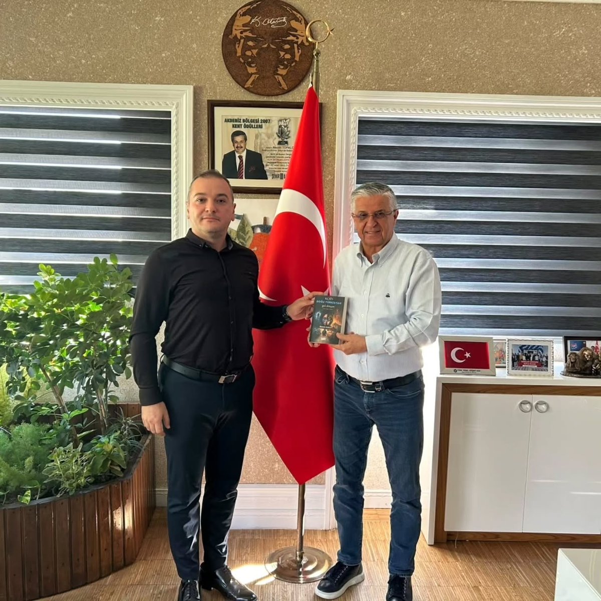 Burak Balıca (left) presenting his book to Kemer Mayor Necati Topaloğlu, October 2026.