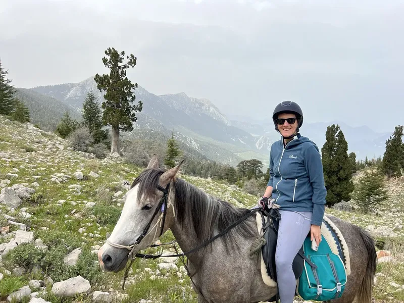 A rider wearing a helmet on a grey horse in a rocky mountain landscape; photograph from Erendiz’s Hilal Ranch image collection.