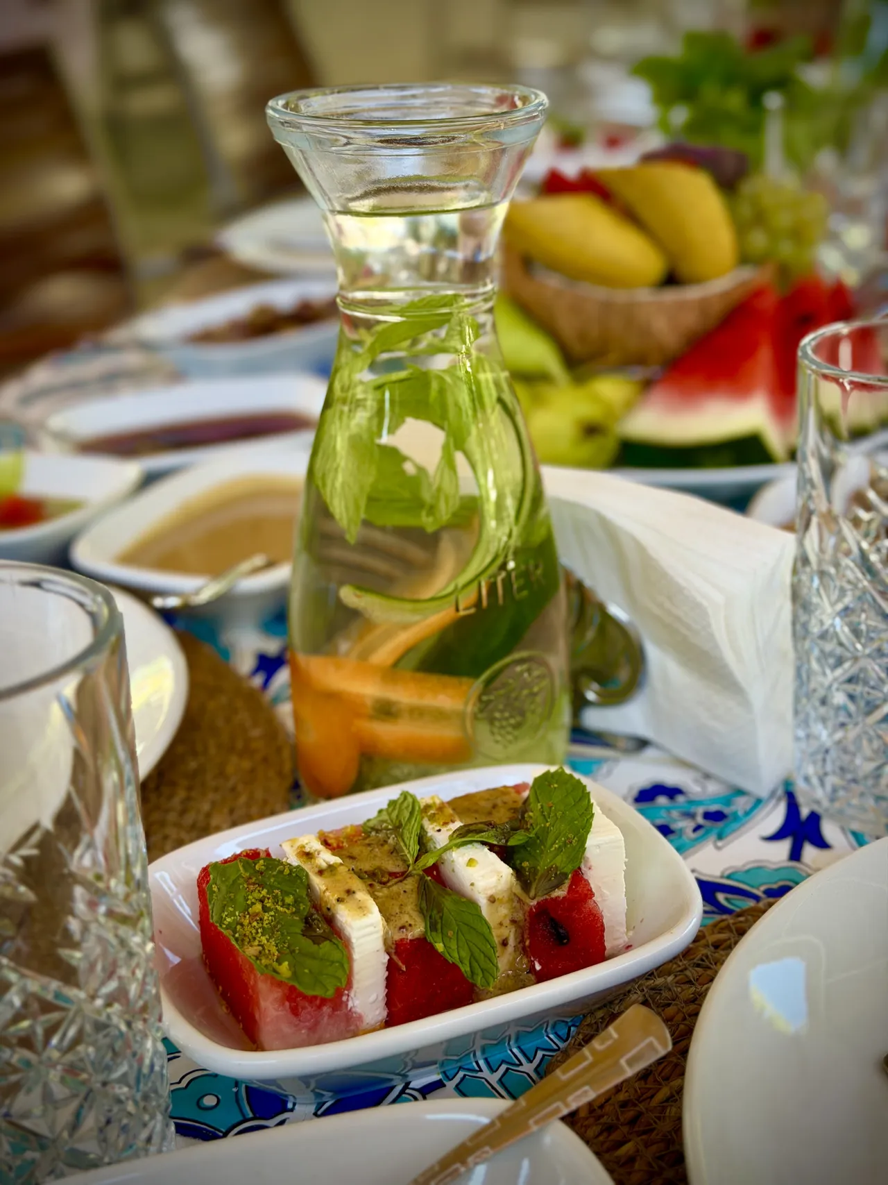 Una caraffa con agrumi ed erbe aromatiche accanto a un piatto di verdure.