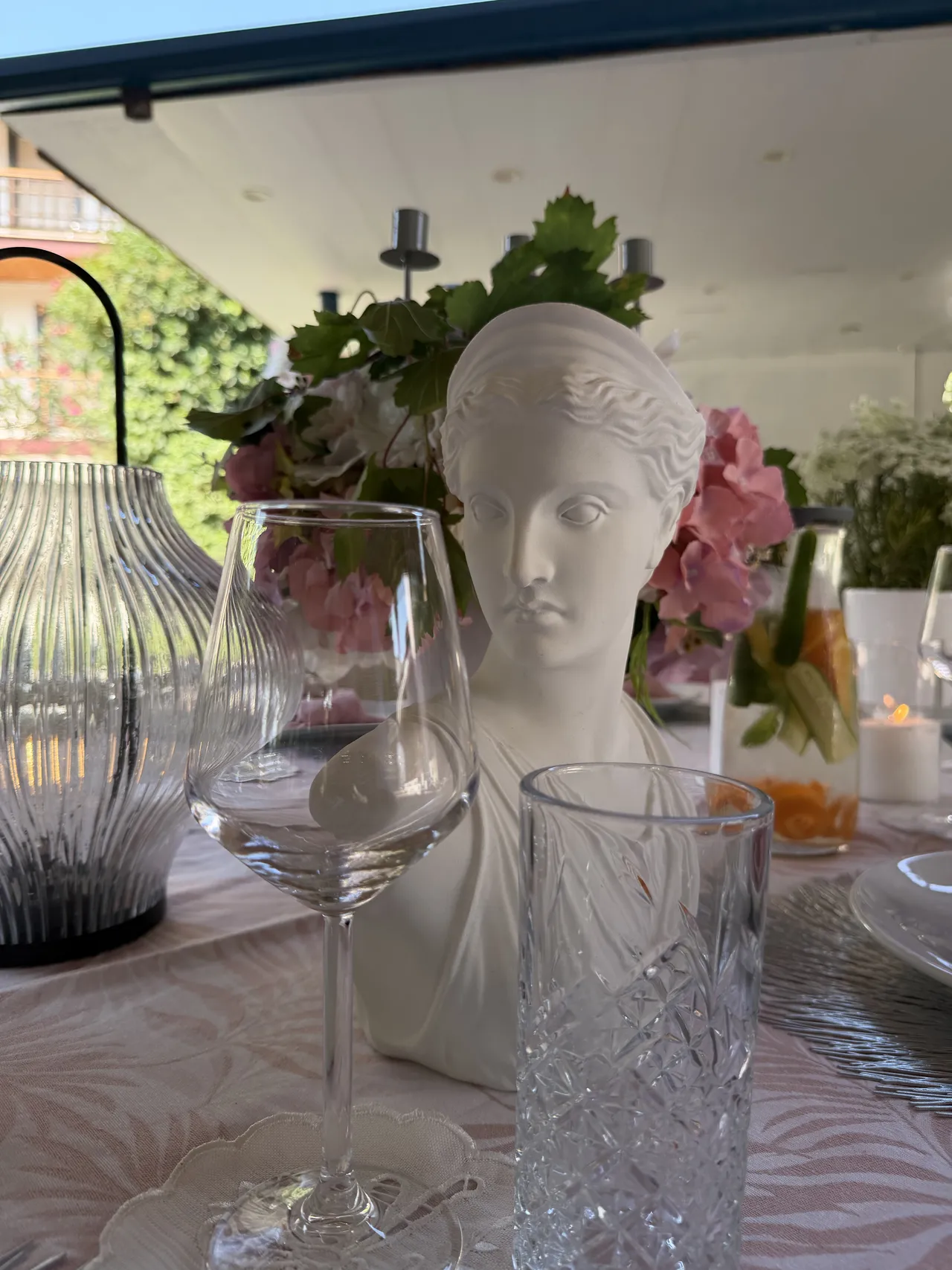 Fiori e un busto decorativo tra i calici della tavola in festa.