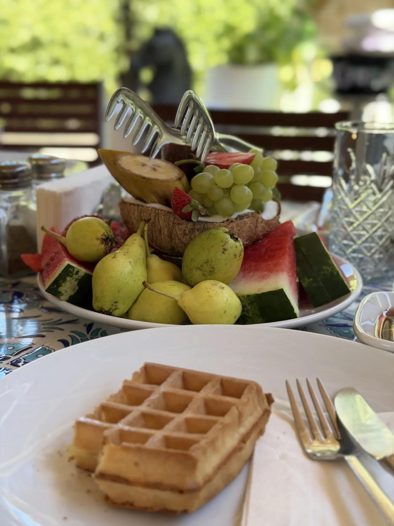 Un waffle sulla tavola apparecchiata, con un vassoio di frutta fresca sullo sfondo.