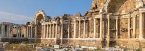 Ancient Roman ruins with a row of tall stone columns and partially preserved arches under a clear blue sky, showcasing historical architecture.